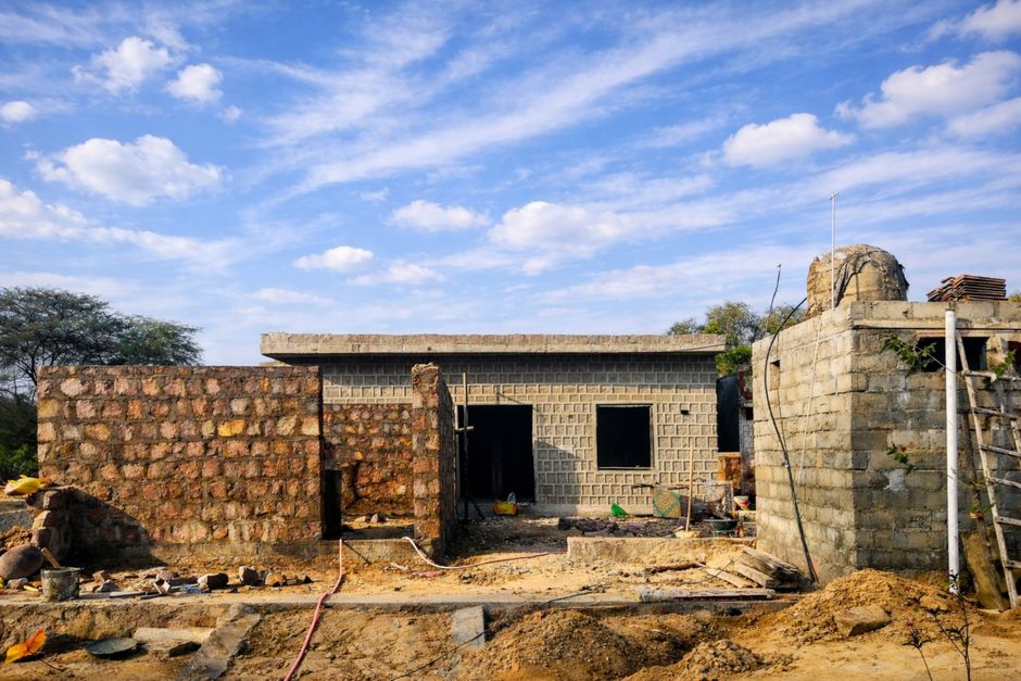 Stone building under construction in a rural area under a bright blue sky.